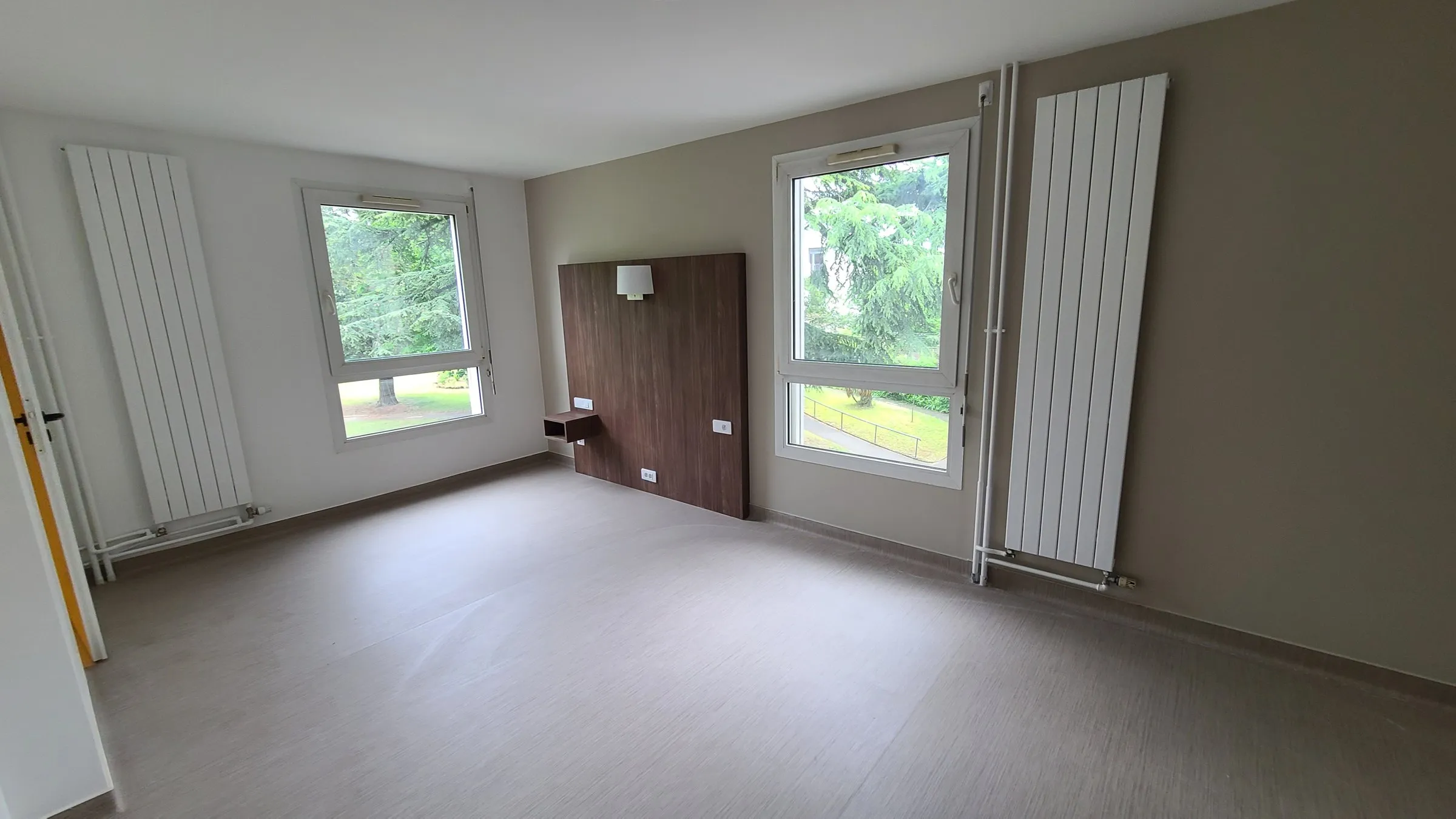 Chambre individuelle rénovée : sol souple, tête de lit bois, deux fenêtres