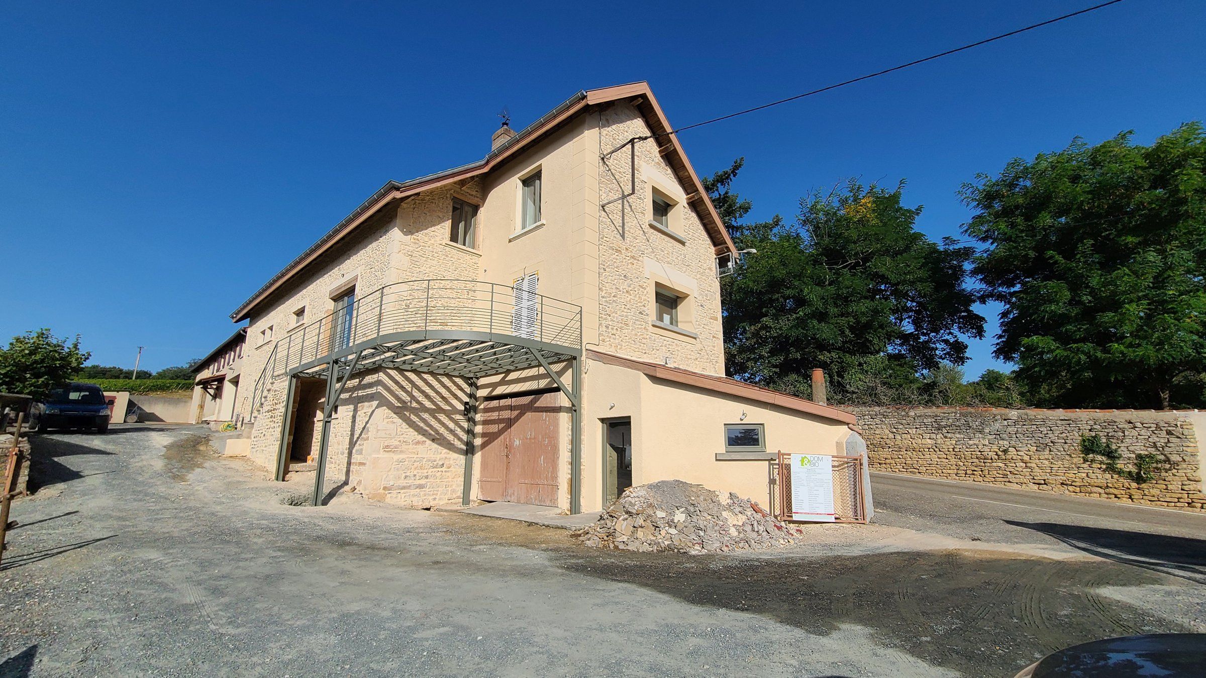 Façade en pierre rénovée d'une bâtisse ancienne, avec un balcon-terrasse métallique